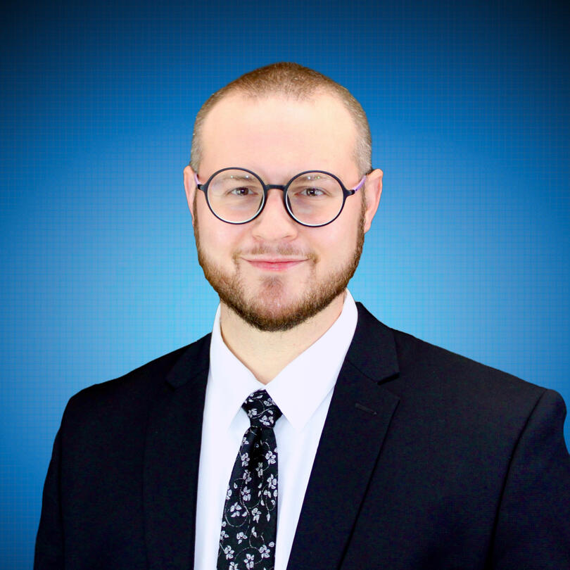 Headshot Headshot of Chanan Brown, a white man wearing round black glasses, a white dress shirt, a black tie with silver flowers, and a black suit jacket. The photo is cropped to a circle and shows Chanan from the chest up in front of a soft blue backdrop.