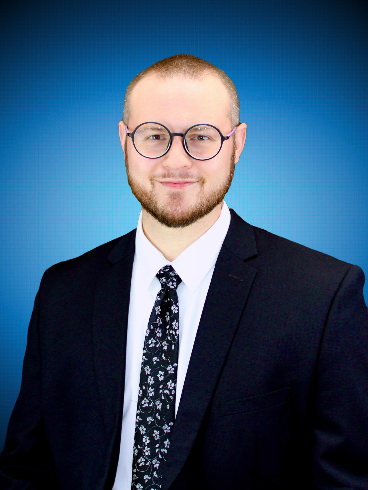 Headshot Headshot of Chanan Brown, a white man wearing round black glasses, a white dress shirt, a black tie with silver flowers, and a black suit jacket. The photo is cropped to a circle and shows Chanan from the chest up in front of a soft blue backdrop.